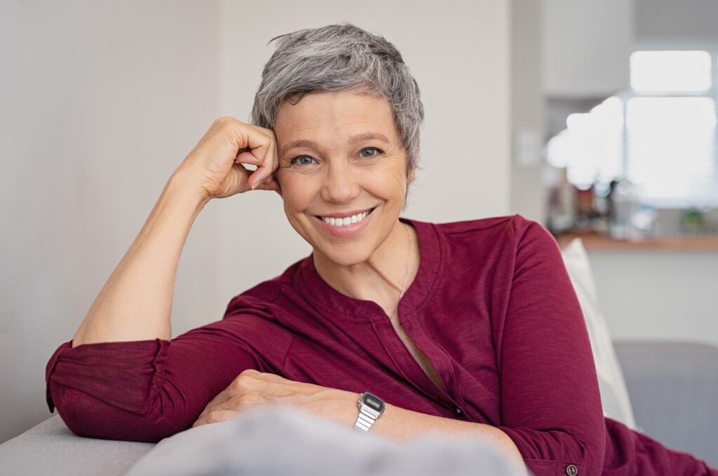 Older woman sitting on the couch smiling.